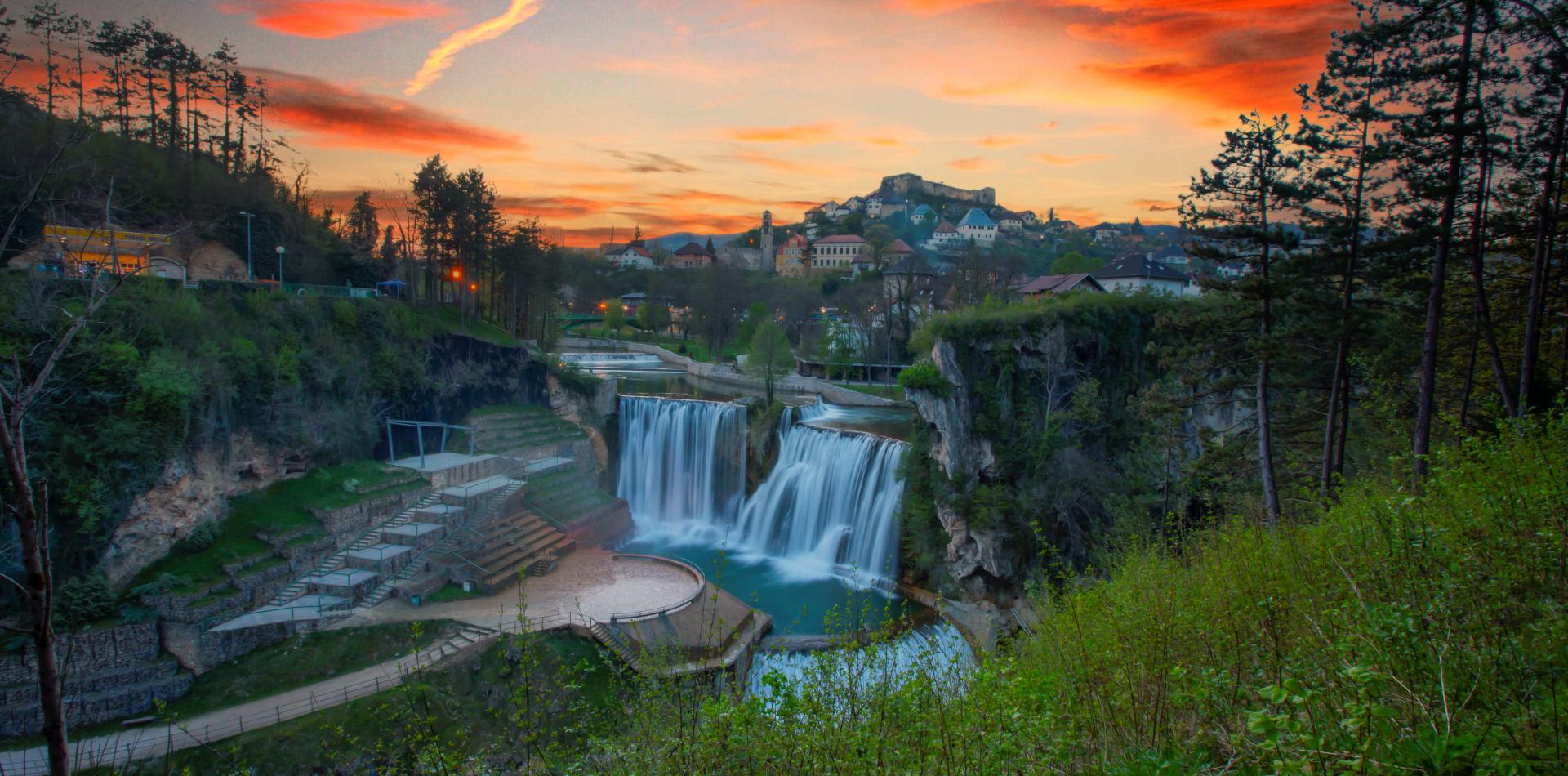 The Pliva Waterfall in Jajce, Bosnia and Herzegovina, with the town’s medieval fortress overlooking the falls at sunset.
